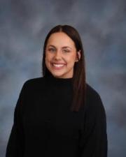 Beth Davis wearing a black, long sleeve shirt and standing in front of a grey backdrop.